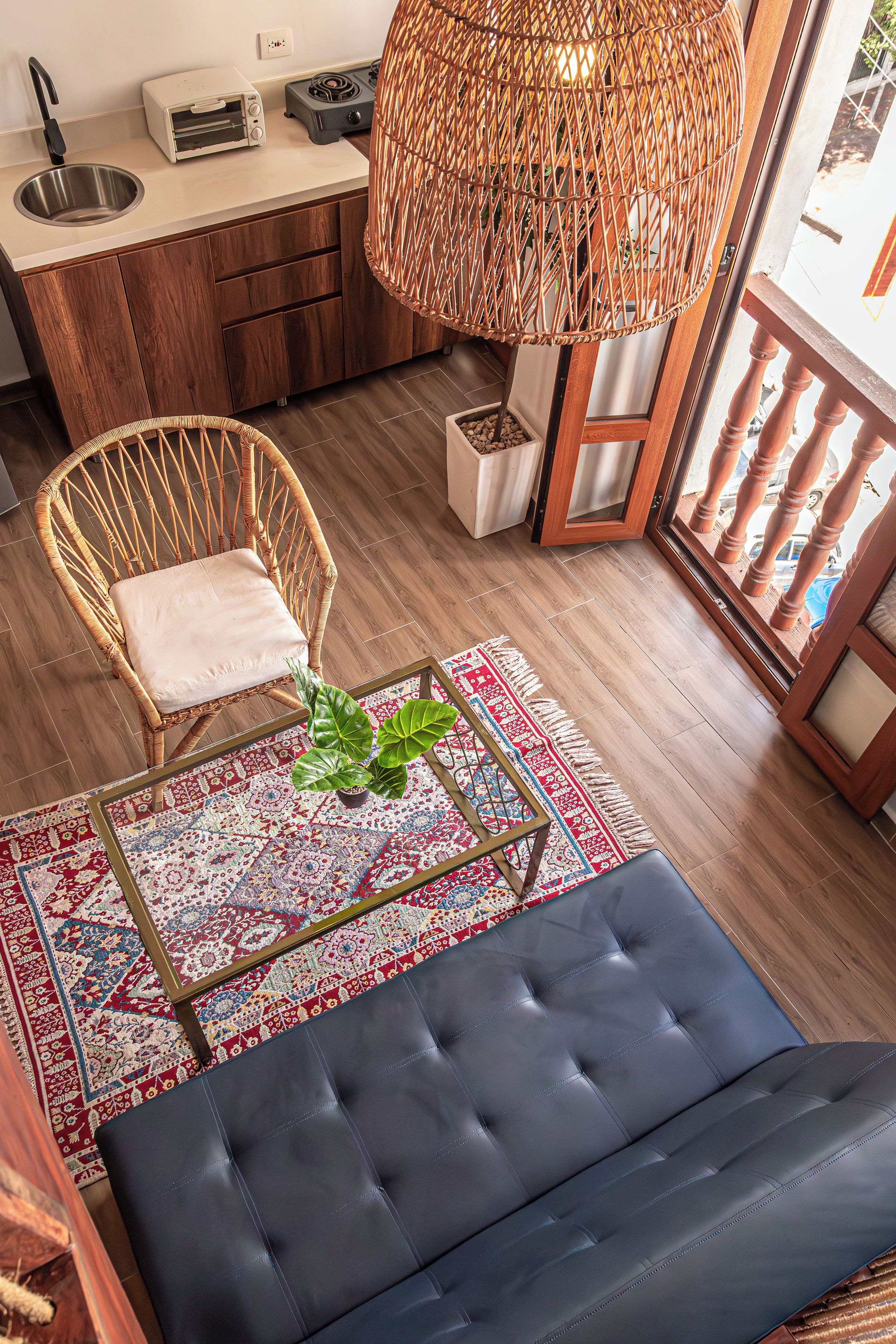 A cozy living area with a sofa, a wicker chair, a dining table with a toaster, and a large woven lamp.