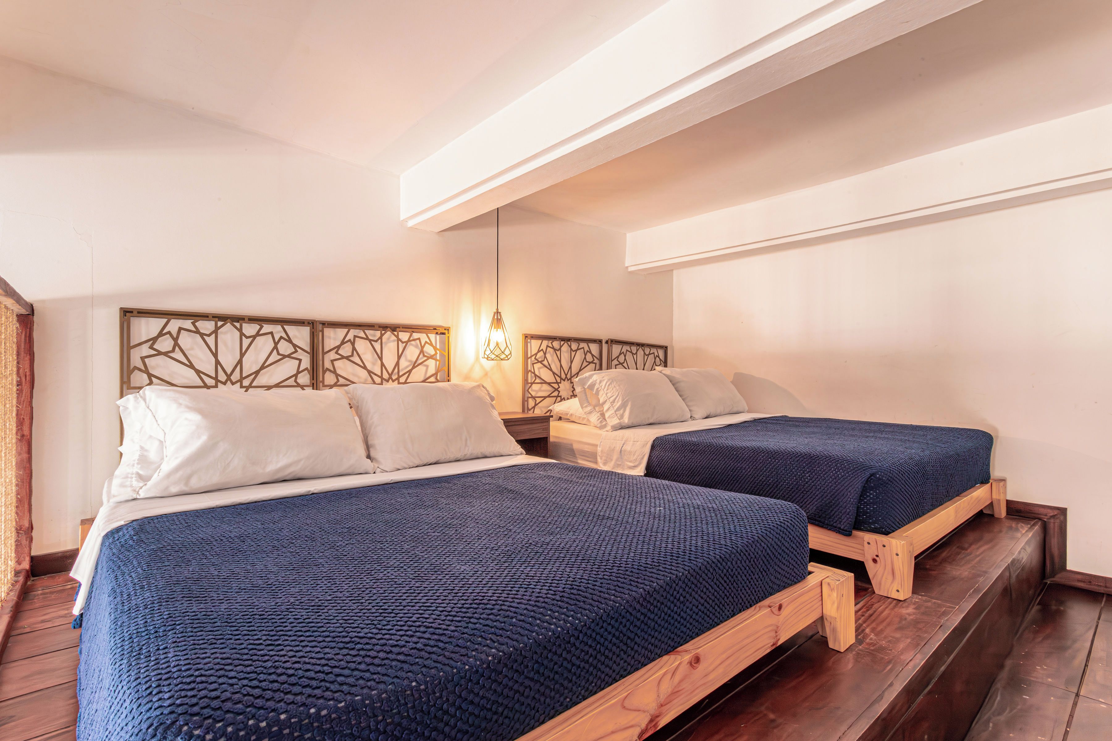 Ein Zimmer mit zwei Betten, Holz-Kopfteilen und einer Hängelampe.