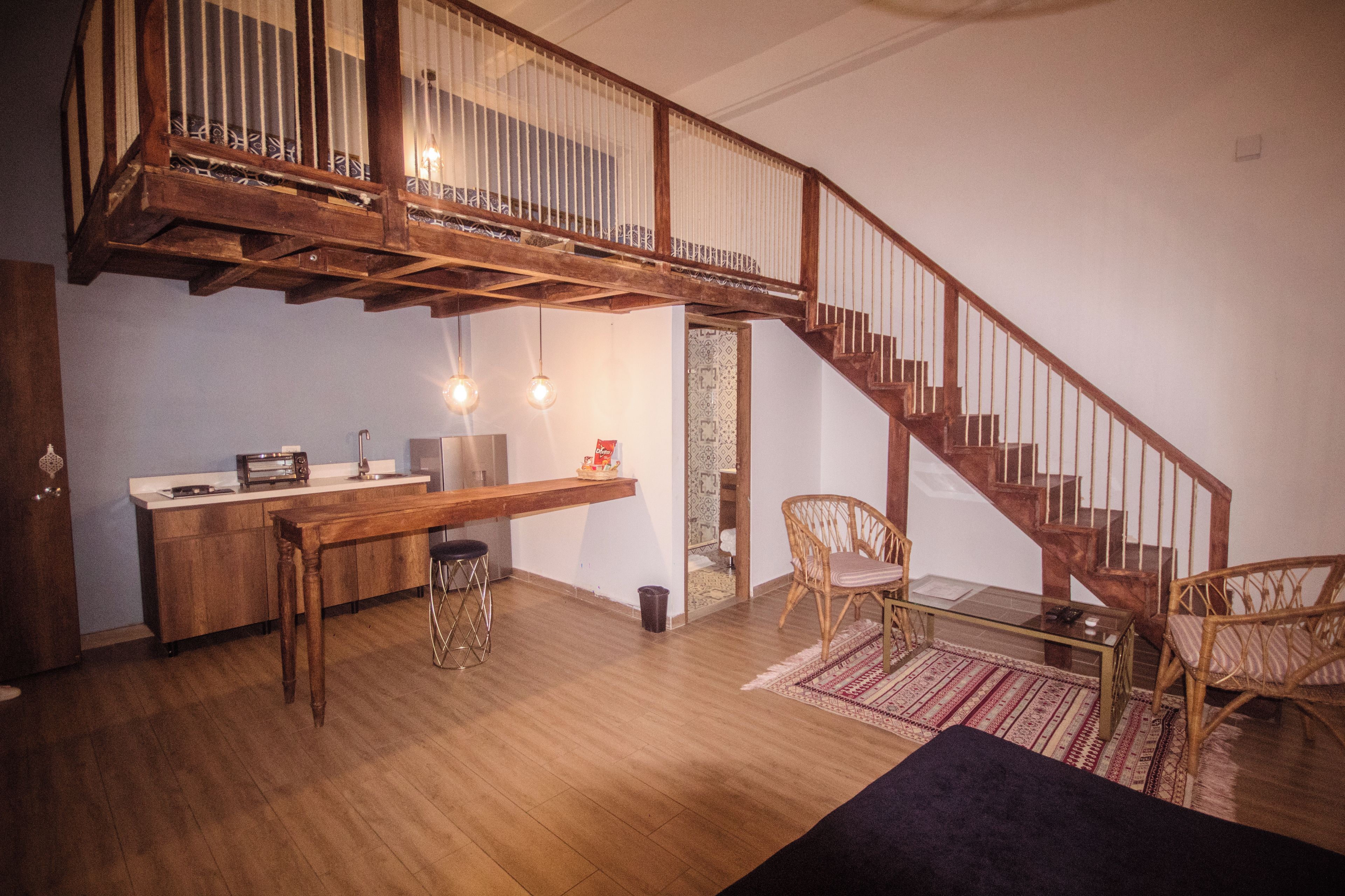 A spacious room with a wooden staircase, a kitchen area, and a seating area with a rug.