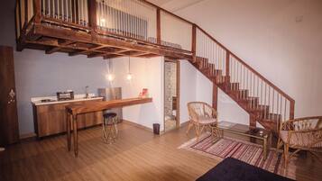 A spacious room with a wooden staircase, a kitchen area, and a seating area with a rug.