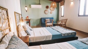 A room with two beds, a blue sofa, wicker chairs, and decorative wall mirrors.