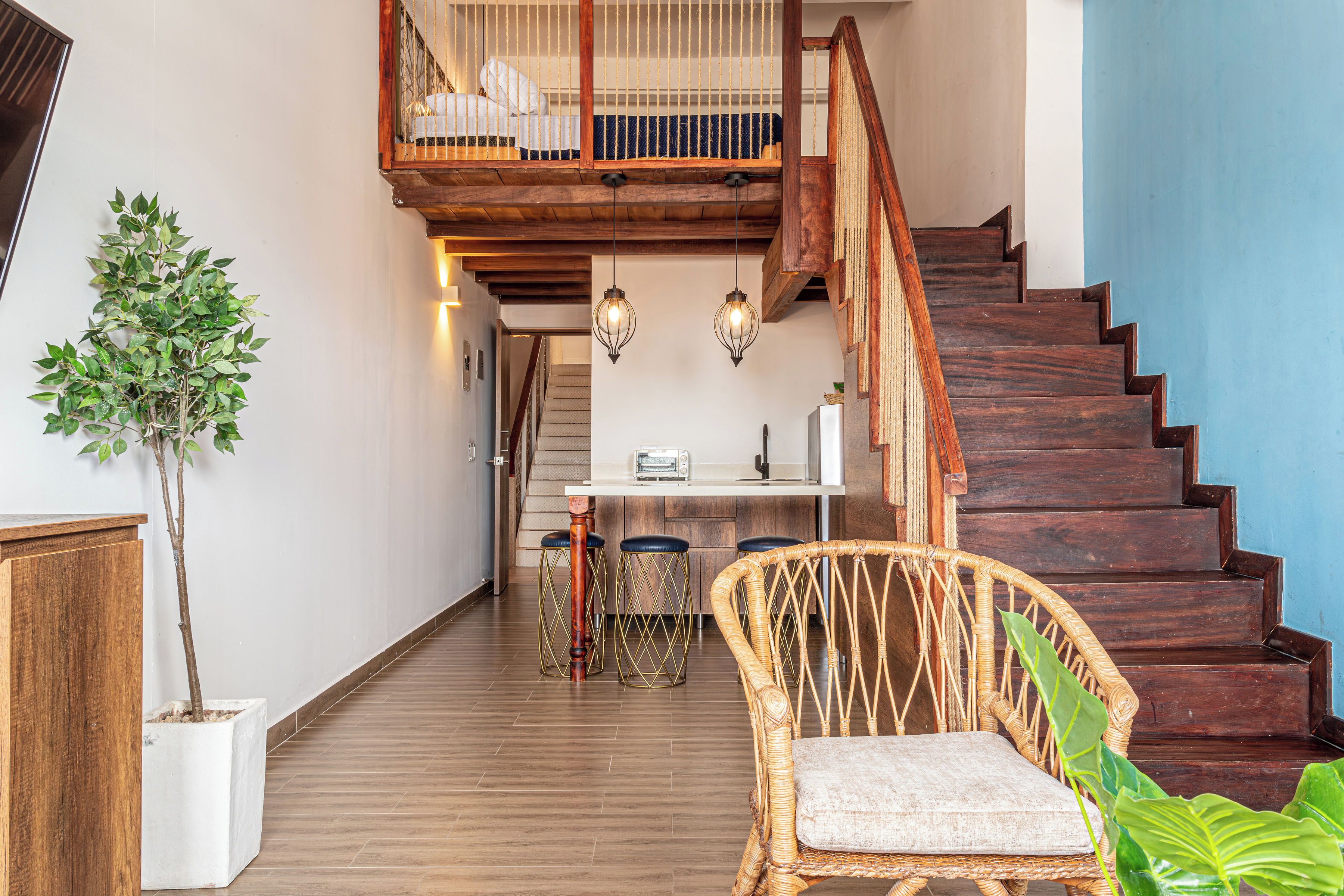 Una escalera de madera lleva a un dormitorio tipo loft con una cama y una lámpara colgante.