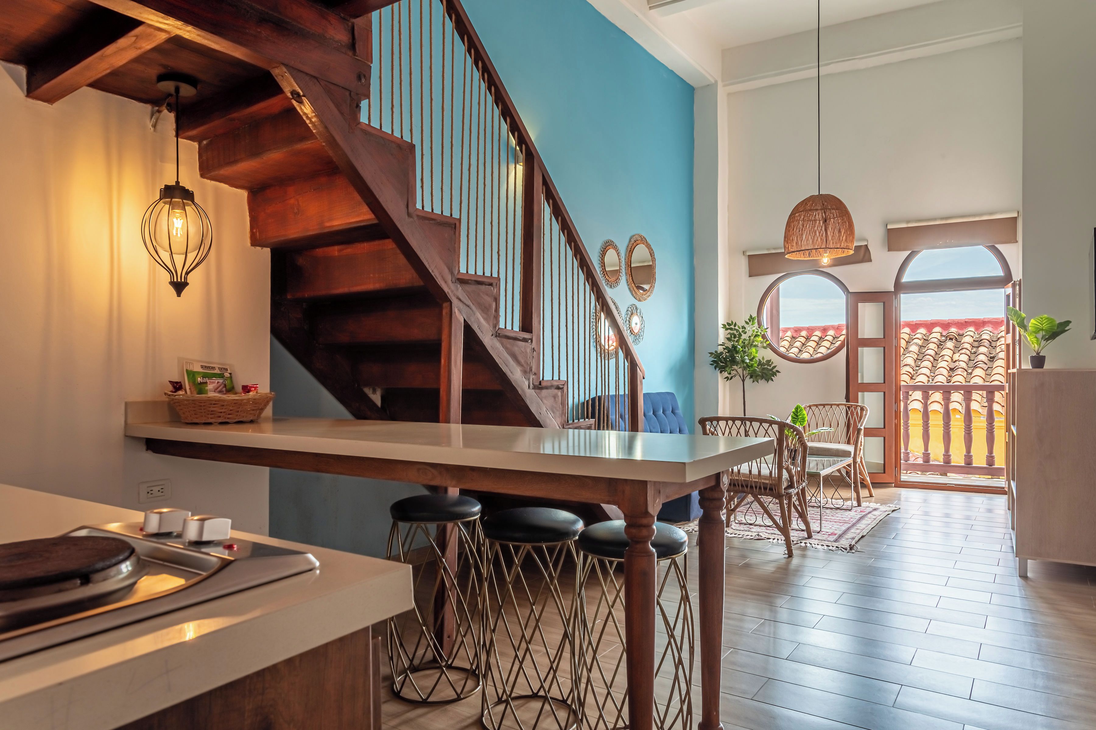 Une cuisine avec un escalier en bois, un coin repas avec des tabourets de bar et une vue sur l’extérieur.