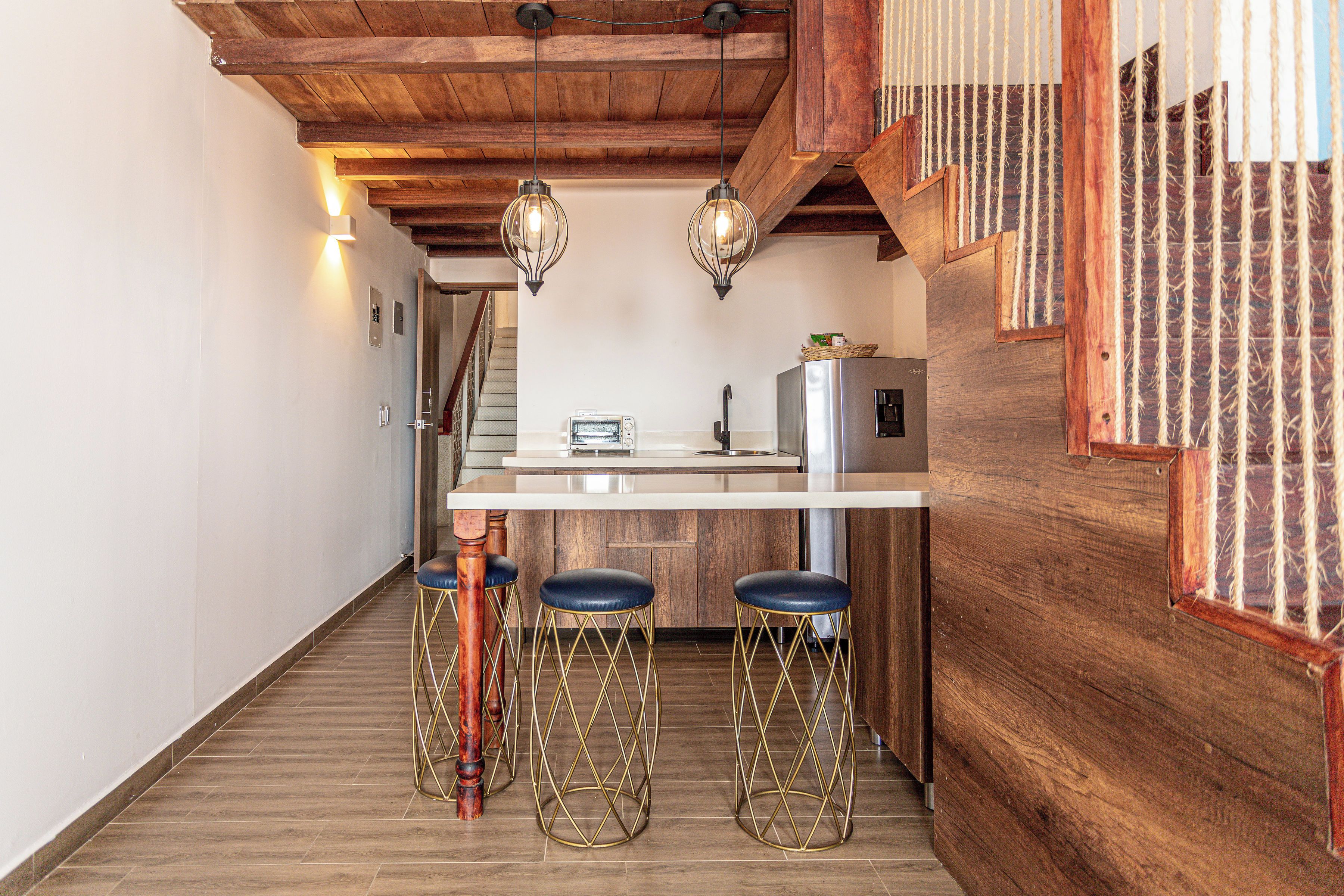 A kitchen with wooden beams, a white countertop, a stainless steel refrigerator, and three stools with gold legs.