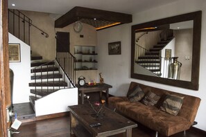 A living room with a brown sofa, a wooden coffee table, a clock, and a staircase with a metal railing. - Dream Villas Antigua (Antigua Guatemala)