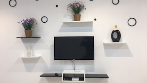 A modern living room with a flat-screen TV mounted on the wall, surrounded by black shelves with decorative items and a white console table.