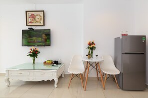 Eine moderne Küche mit einem weißen Tisch, zwei weißen Stühlen, einer Glastischplatte, einem Kühlschrank, einem Fernseher und einem gerahmten Bild an der Wand.