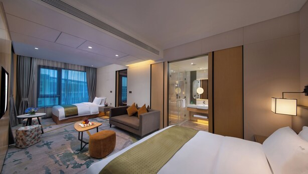 A hotel room with a large bed, a sofa, a small table, and a glass shower area. - Holiday Inn Hangzhou Airport Zone by IHG (Hangzhou)
