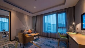 A hotel room with a sofa, armchair, desk, and large windows. - Holiday Inn Hangzhou Airport Zone by IHG (Hangzhou)