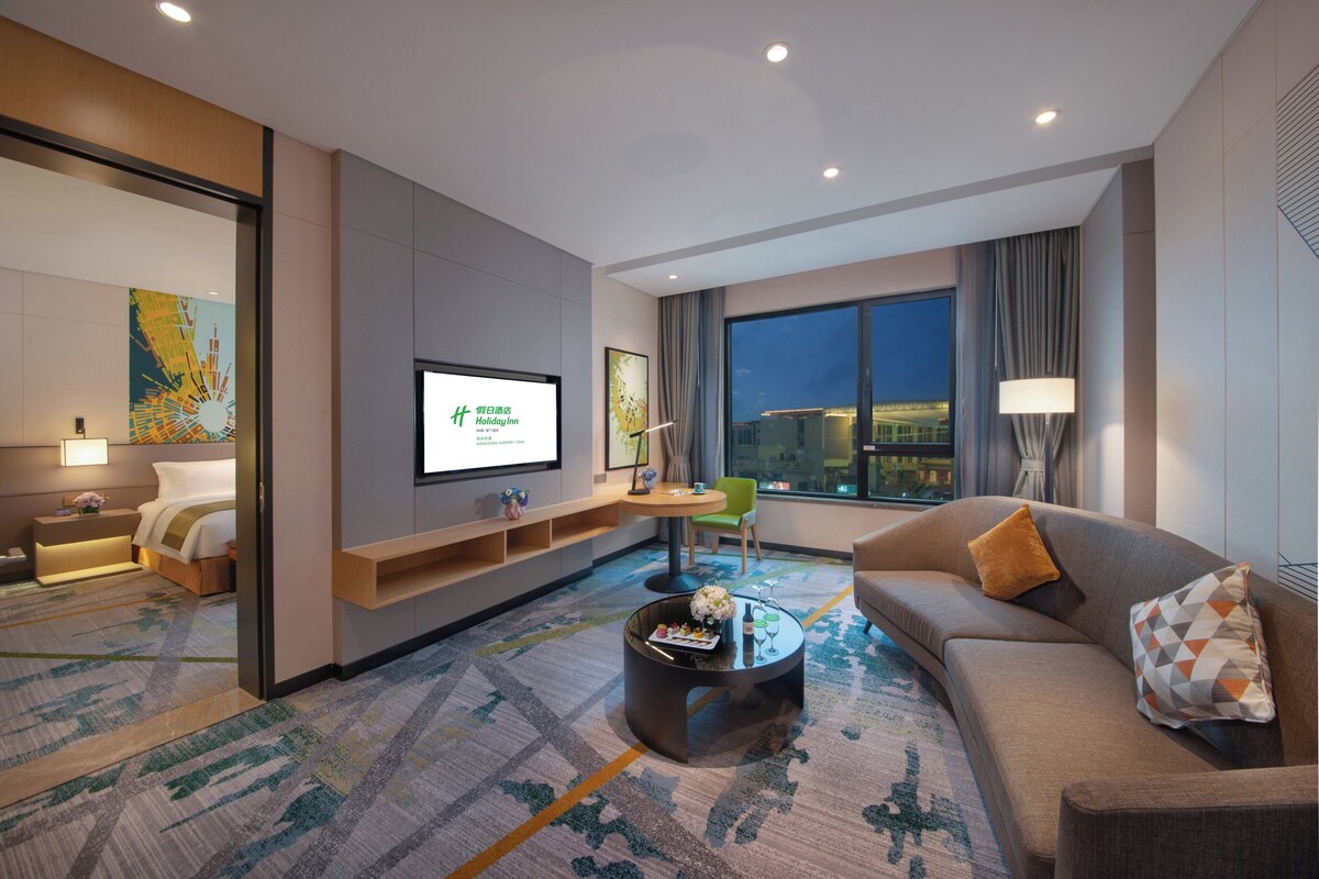 A modern hotel room with a large bed, a sofa, a coffee table, and a TV.