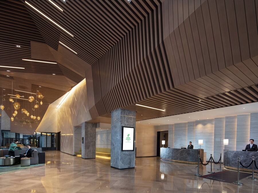 En rymlig entréhall med modern design, med en receptionsdisk, sittgrupp och ett unikt mönster i taket.
