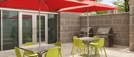 Un patio al aire libre con mesa y sillas, una parrilla y sombrillas rojas.