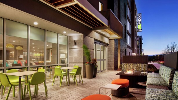An outdoor seating area with green chairs and orange ottomans, a fire pit, and a view of the city at dusk. - Home2 Suites by Hilton Silver Spring (Silver Spring)