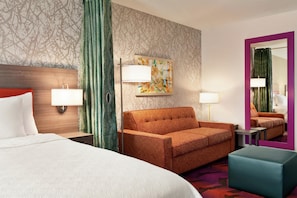 Ein Hotelzimmer mit einem Bett, einer Couch, einem kleinen Tisch, einer Lampe und einem Gemälde an der Wand.
