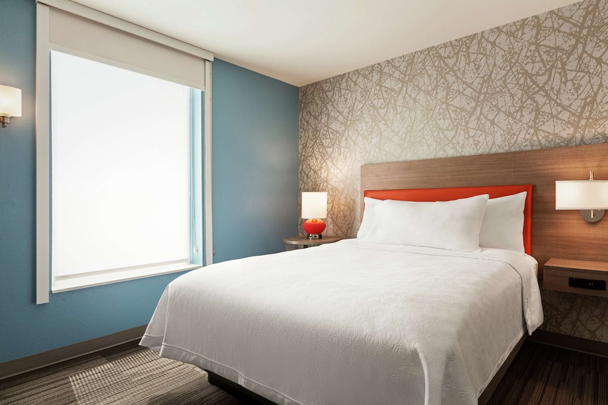 A hotel room with a large bed, two bedside lamps, a window, and a patterned wall.
