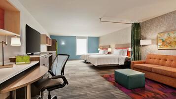 A hotel room with a desk, two beds, a sofa, and a TV.