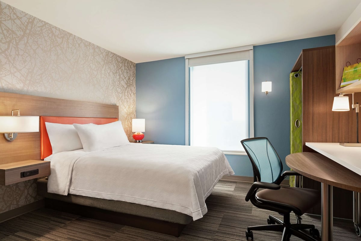 A hotel room with a bed, a desk, a chair, and a window.