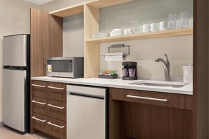 Una cocina moderna con refrigerador, microondas, lavavajillas y un lavamanos con grifo.