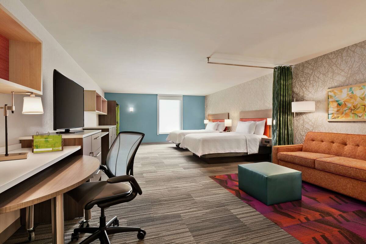 A hotel room with a desk, two beds, a sofa, and a TV.