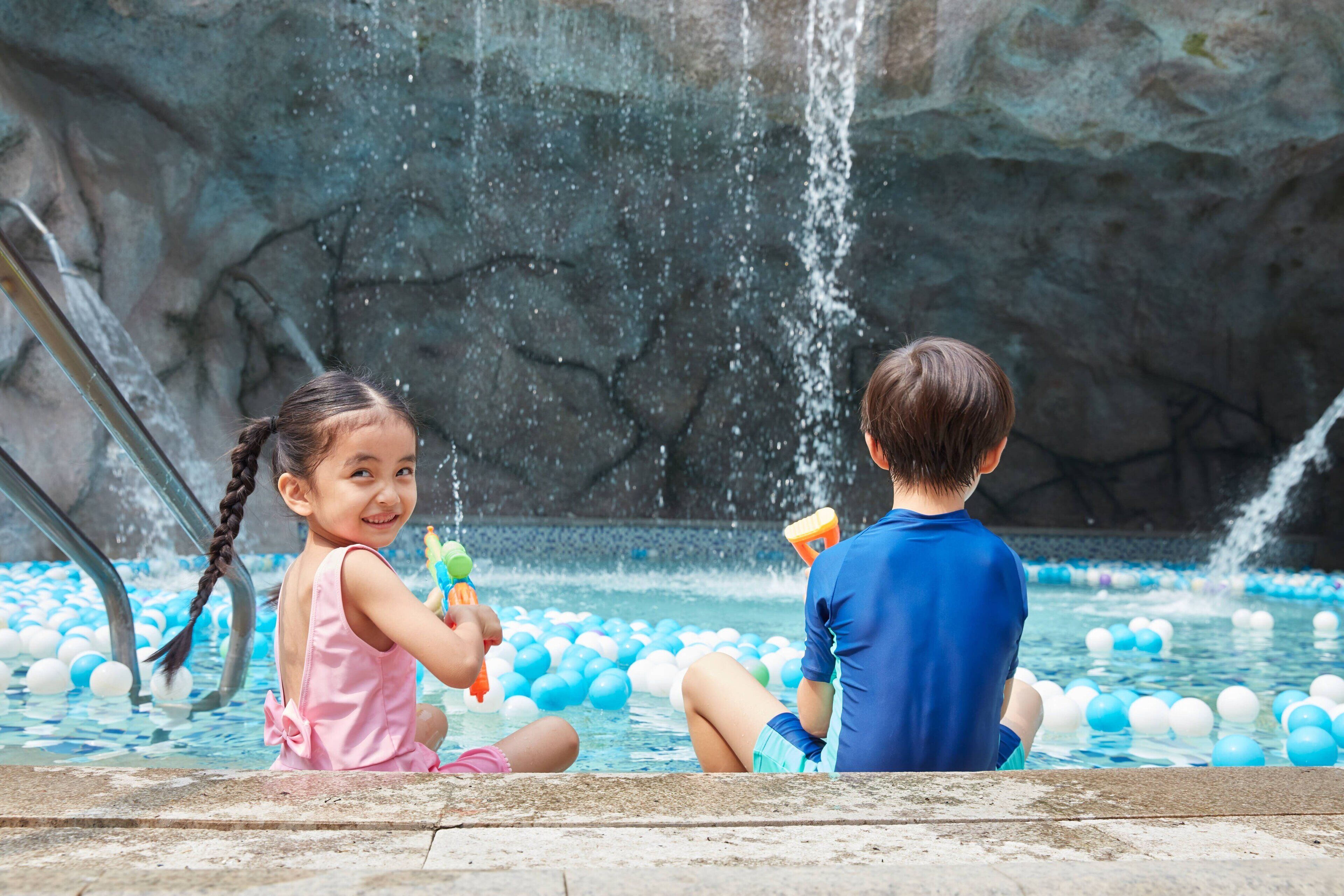 Two children playing in a water play area with a rock wall in the background.