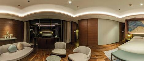 A modern hotel room with a curved ceiling, wooden flooring, a sofa set, a small round table, and a bed with a headboard.