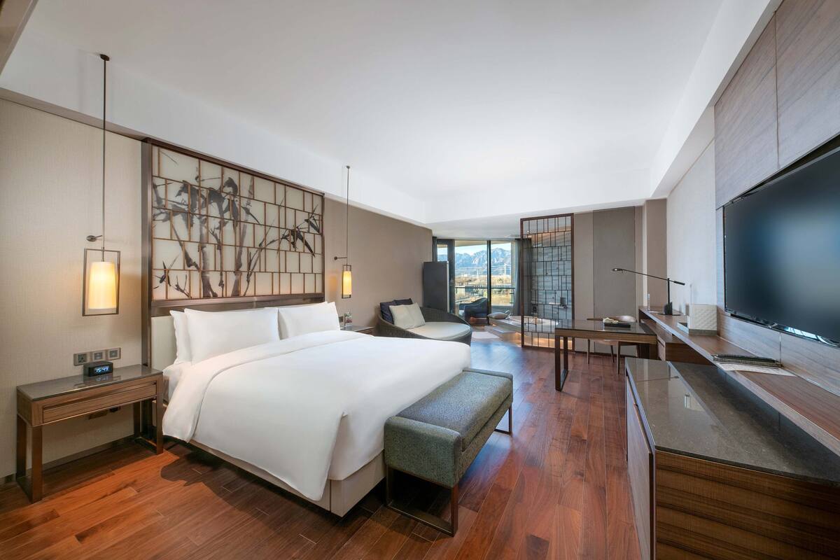 A modern hotel room with a large bed, a desk, a chair, and a TV.