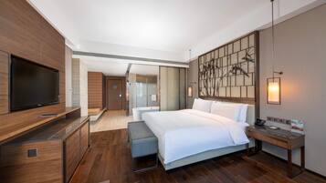A modern hotel room with a large bed, a TV, a desk, and a bathroom visible through an open door.
