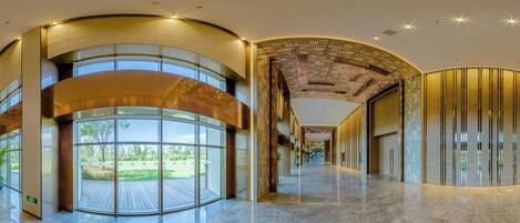 A spacious, modern lobby with curved glass walls, a marble floor, and a ceiling with a unique pattern.