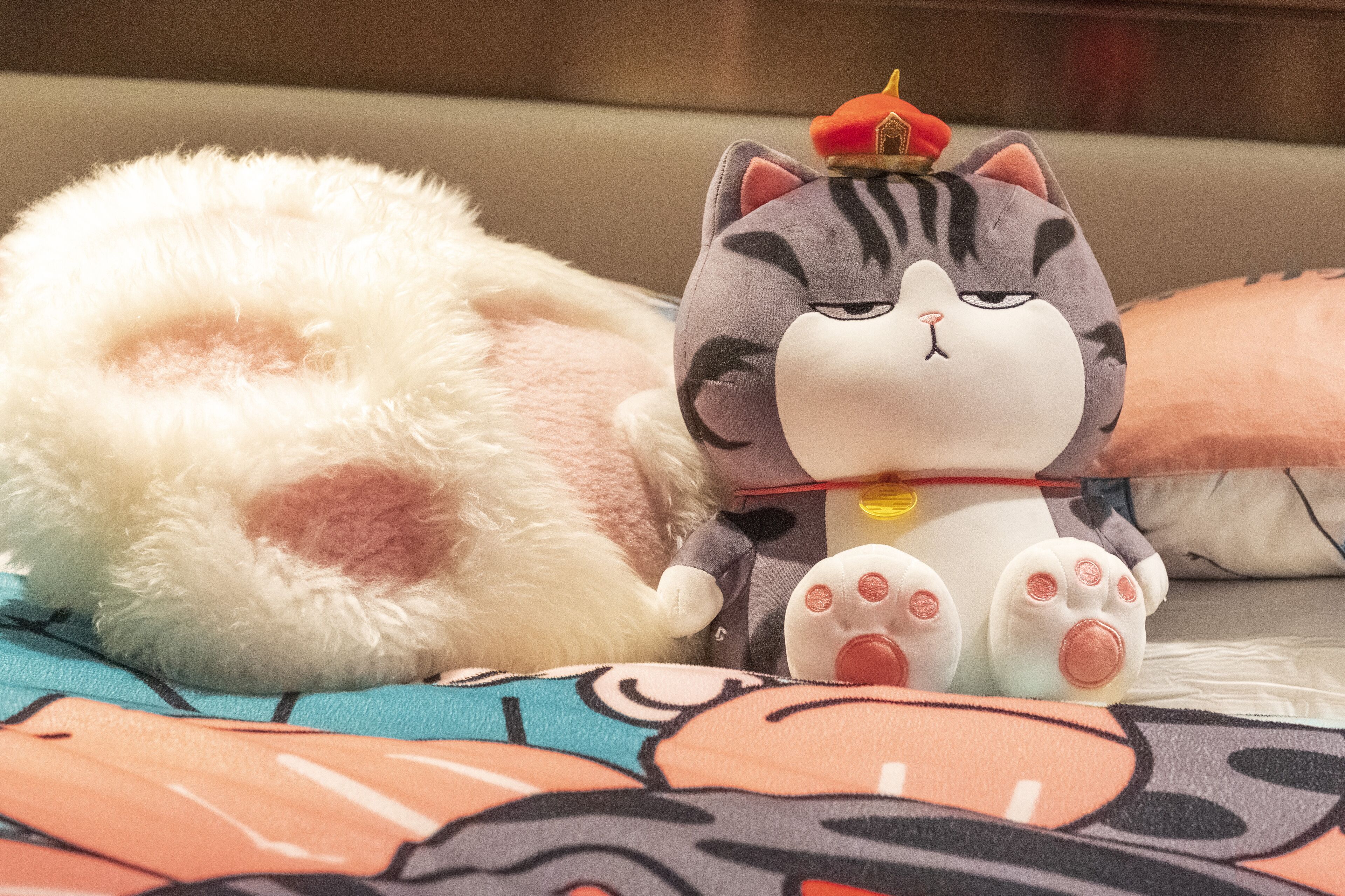 Un gato y un perro de peluche sobre una cama con una manta estampada.