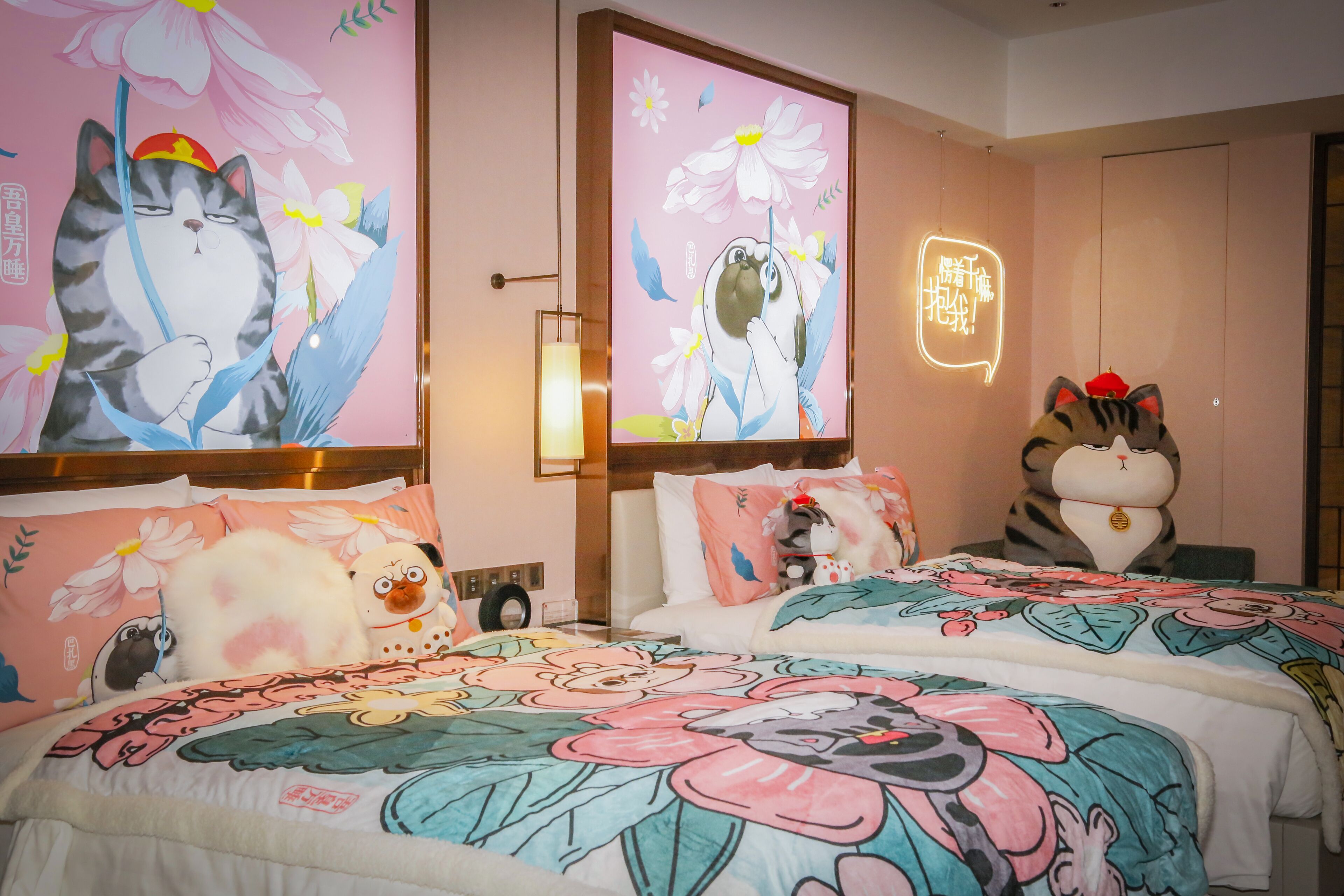 Quarto de hotel com duas camas, cada uma com roupa de cama estampada com flores e um grande mural na parede de um gato.