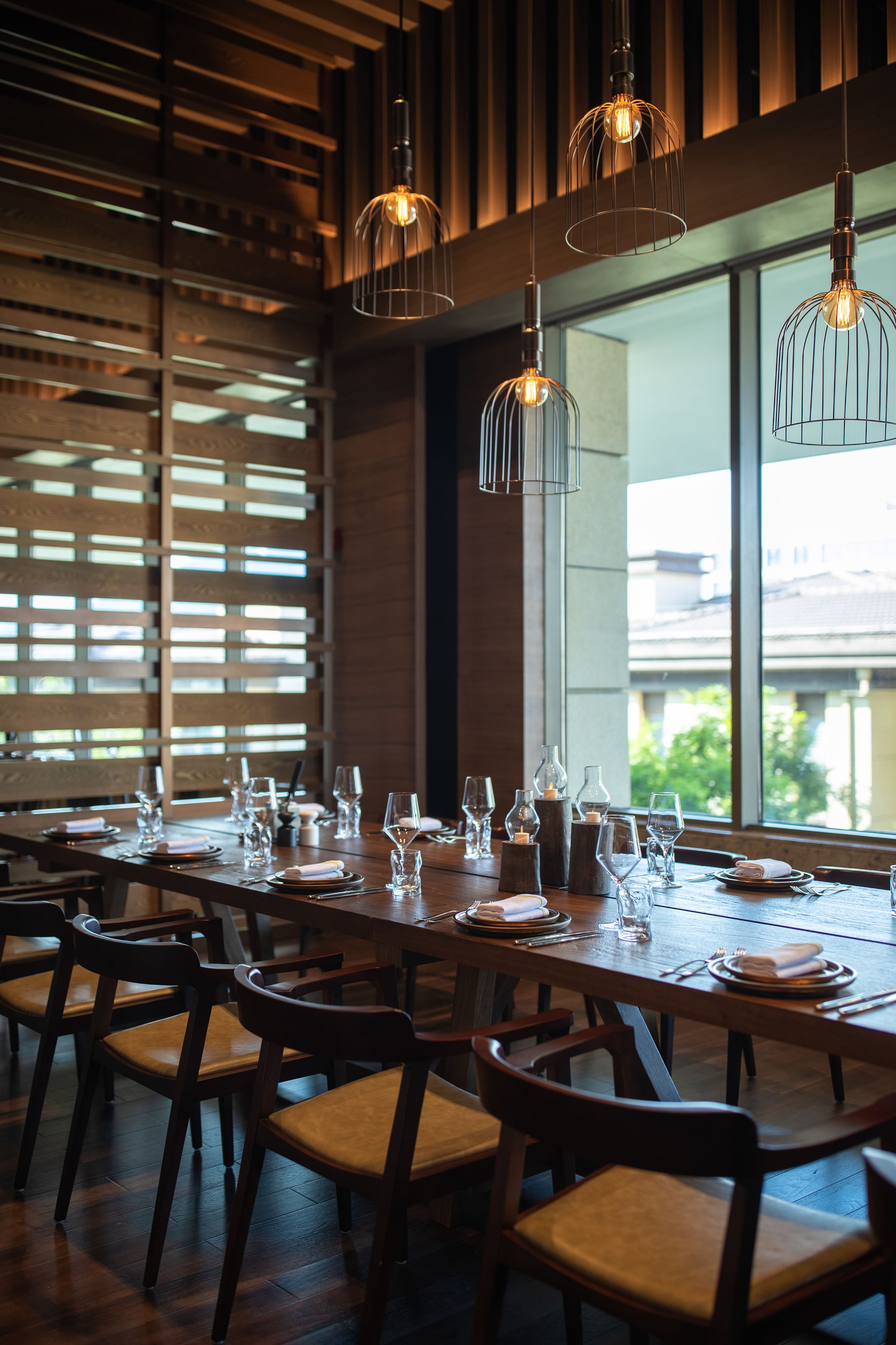 Un comedor con una larga mesa dispuesta para una comida, sillas de madera y lámparas colgantes.