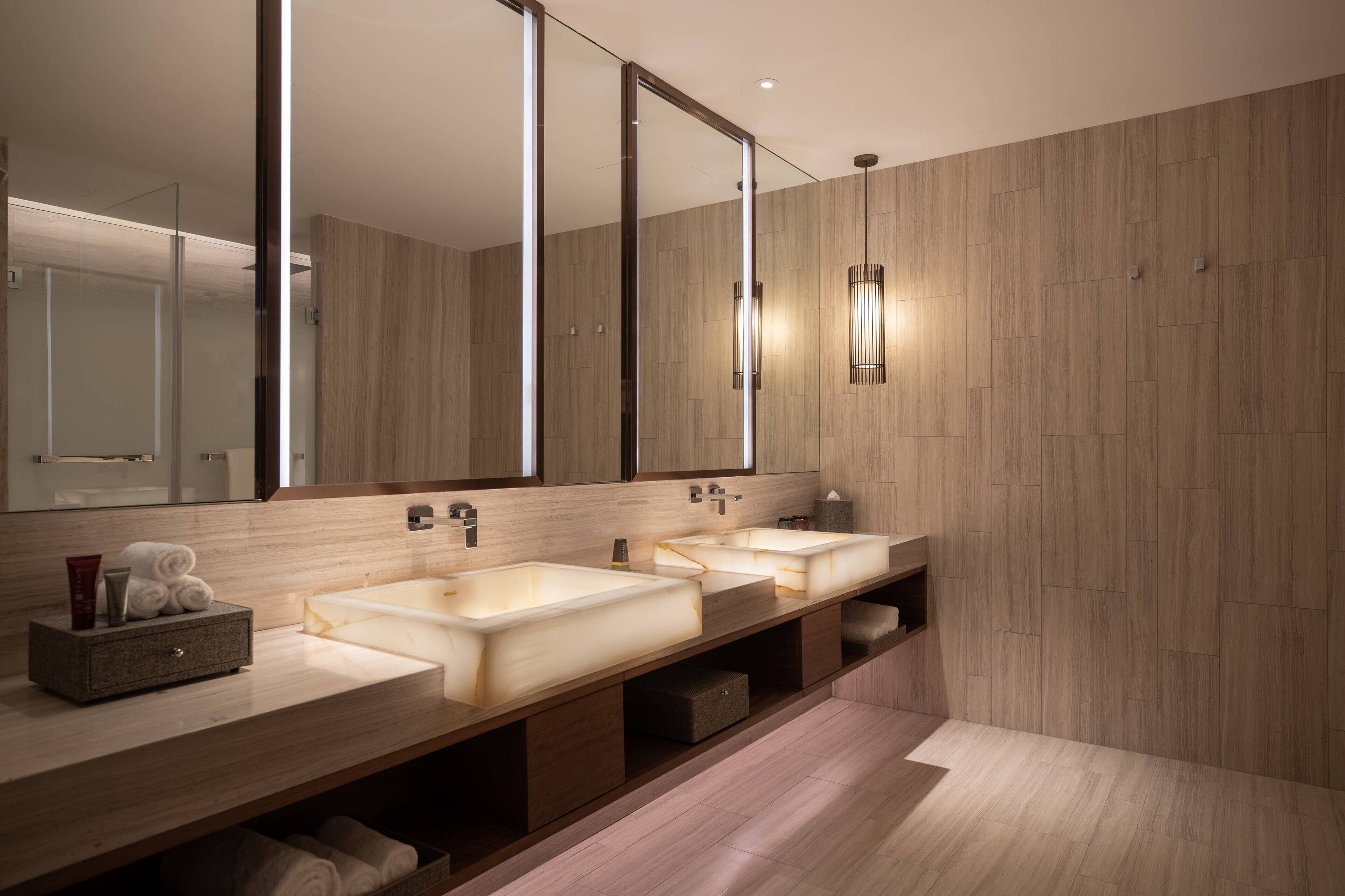 A modern bathroom with three sinks, a large mirror, and a wooden vanity.