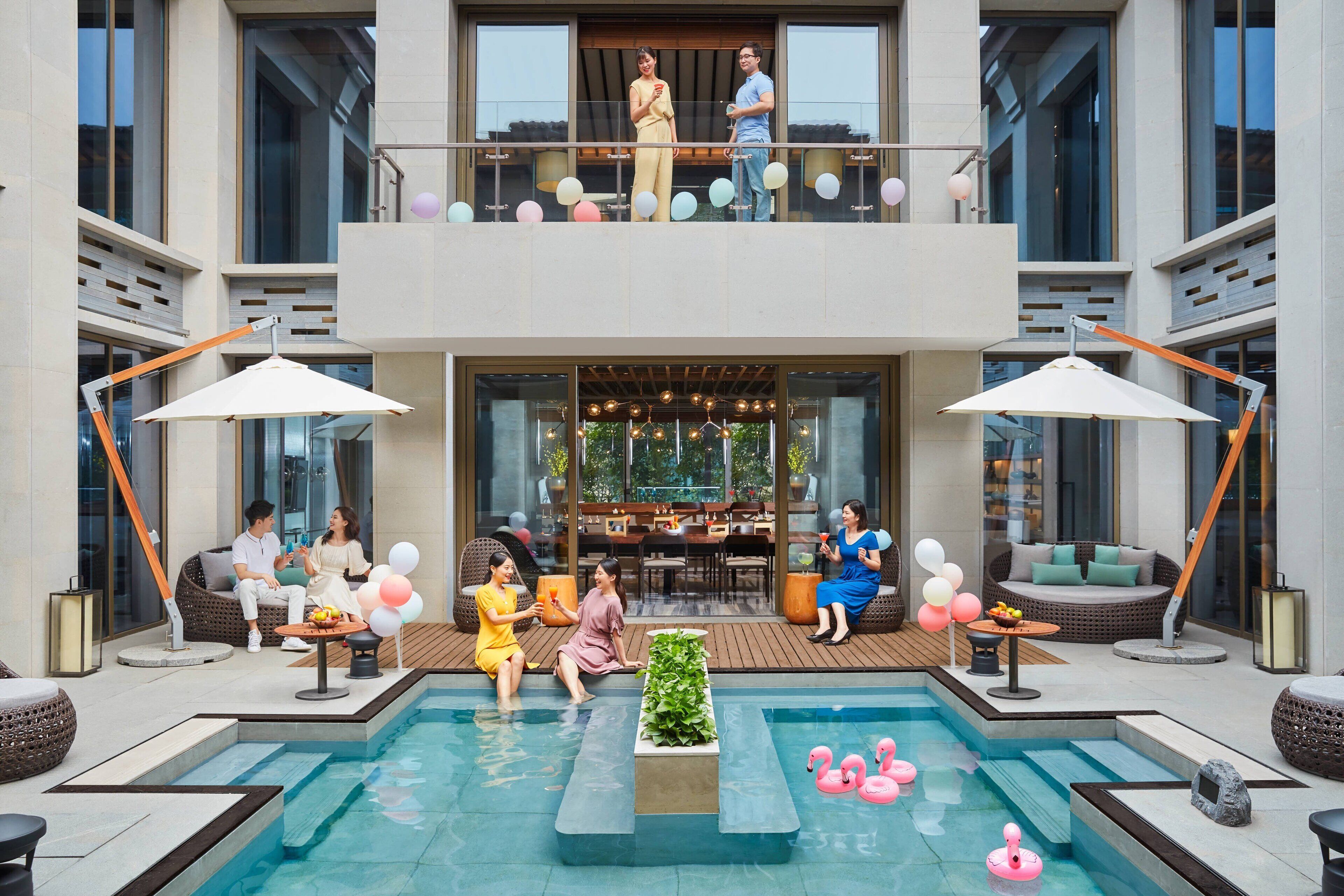 Un hotel moderno con zona de piscina, asientos al aire libre y un balcón decorado con globos.