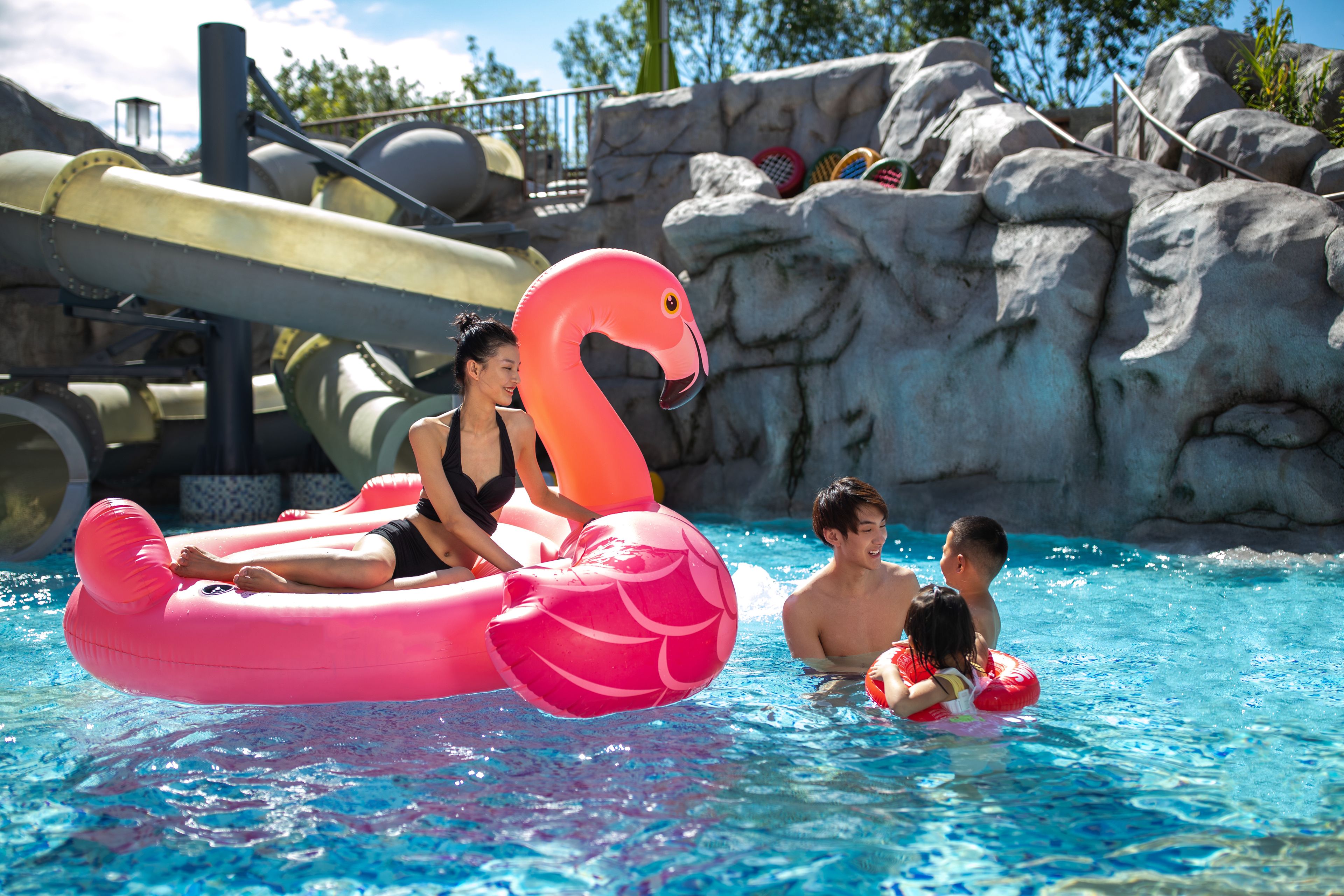En pool med oppustelige flamingoer og et vandrutsjebane i baggrunden.
