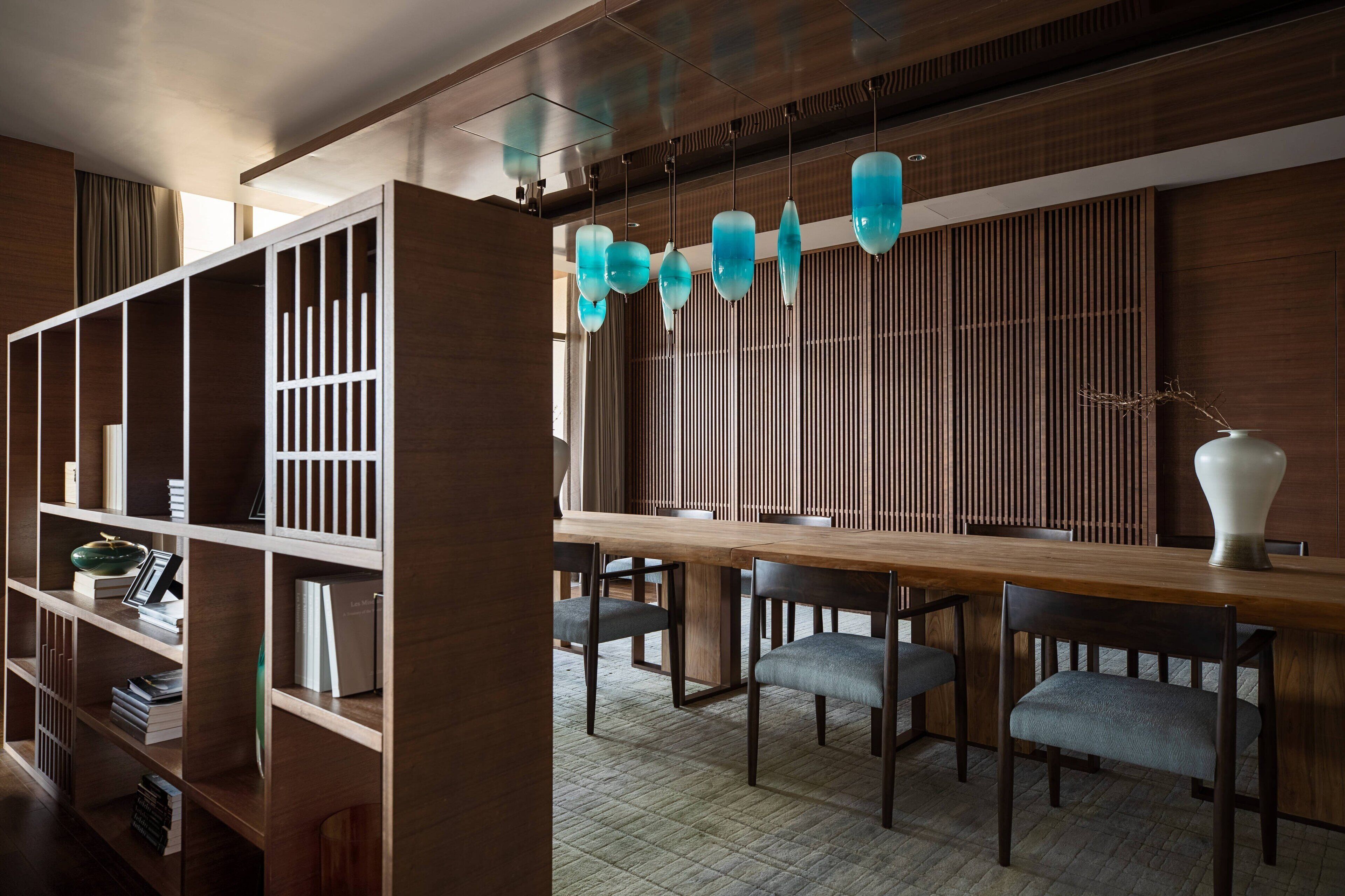 A modern dining area with a wooden table and chairs, a bookshelf, and a decorative hanging light fixture.