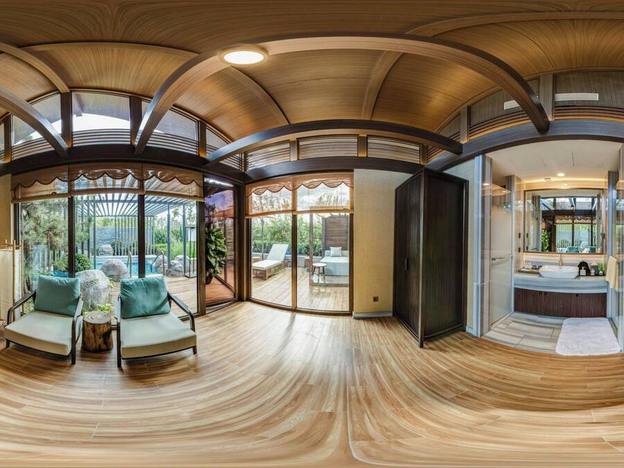 A spacious room with a curved wooden ceiling, large sliding glass doors leading to an outdoor area with a pool, and a modern bathroom with a large mirror and sink.