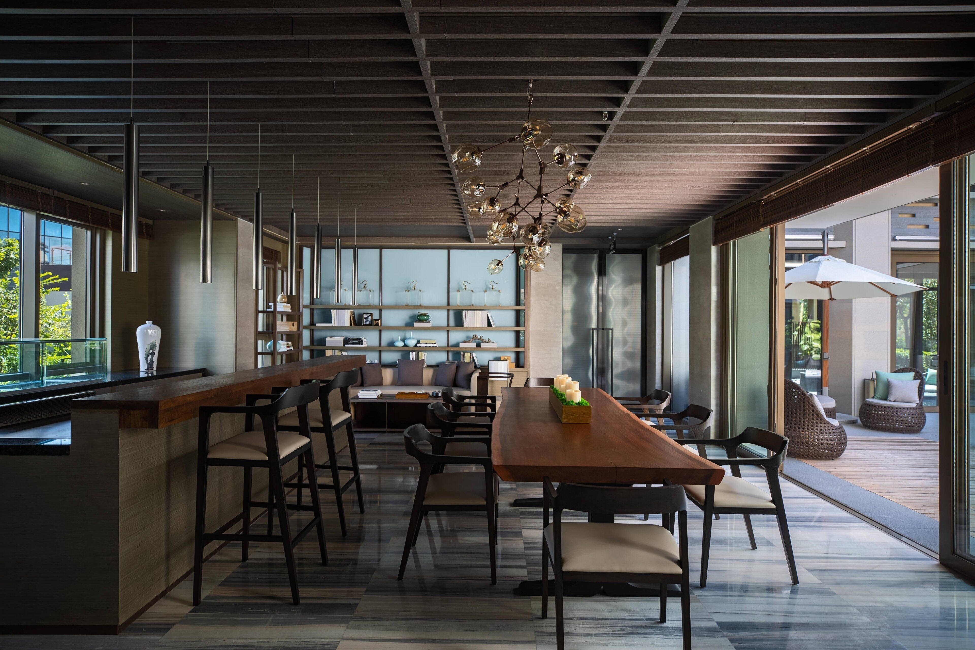 Una cocina moderna con una isla de madera, taburetes de bar y una mesa de comedor con sillas. Una ventana grande ofrece vistas al exterior.