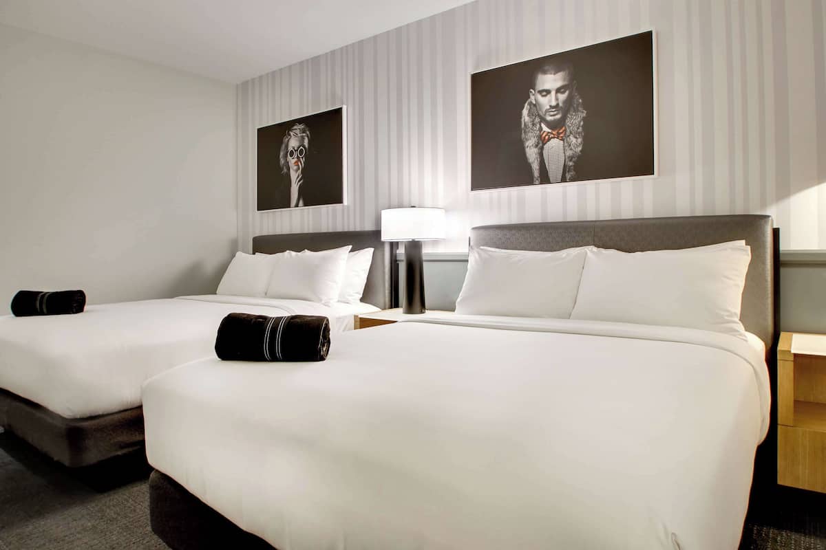 A hotel room with two beds, a nightstand, a lamp, and two framed pictures on the wall.
