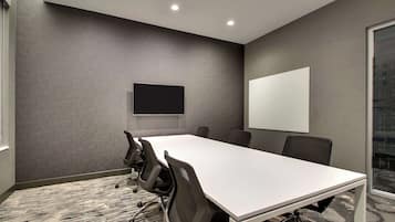 Una sala de conferencias con una larga mesa, sillas, un televisor de pantalla plana y una pizarra.