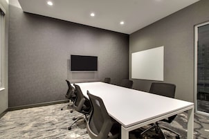 Una sala de conferencias con una larga mesa, sillas, un televisor de pantalla plana y una pizarra.