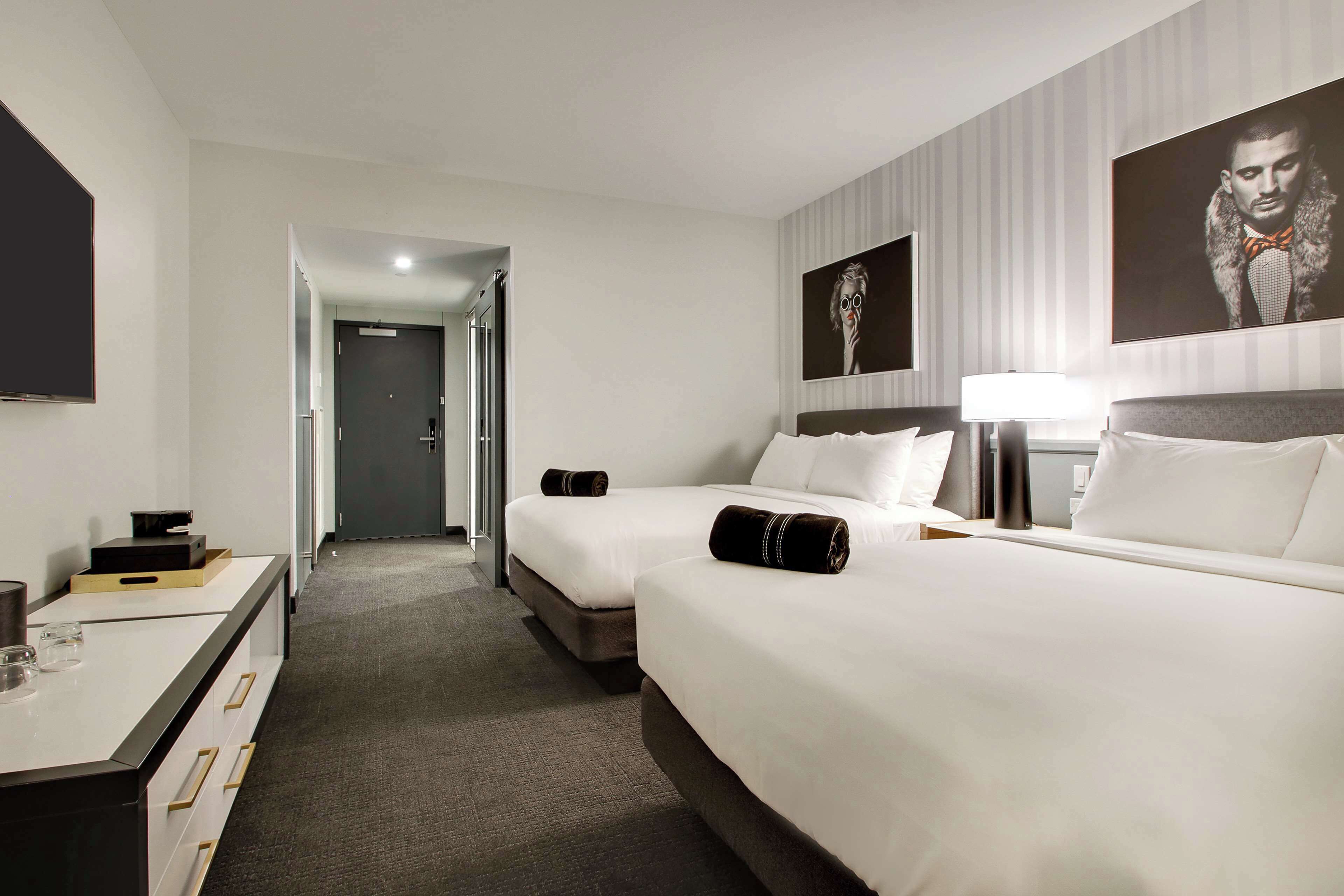 A hotel room with two beds, a desk, a lamp, and a large framed picture on the wall.