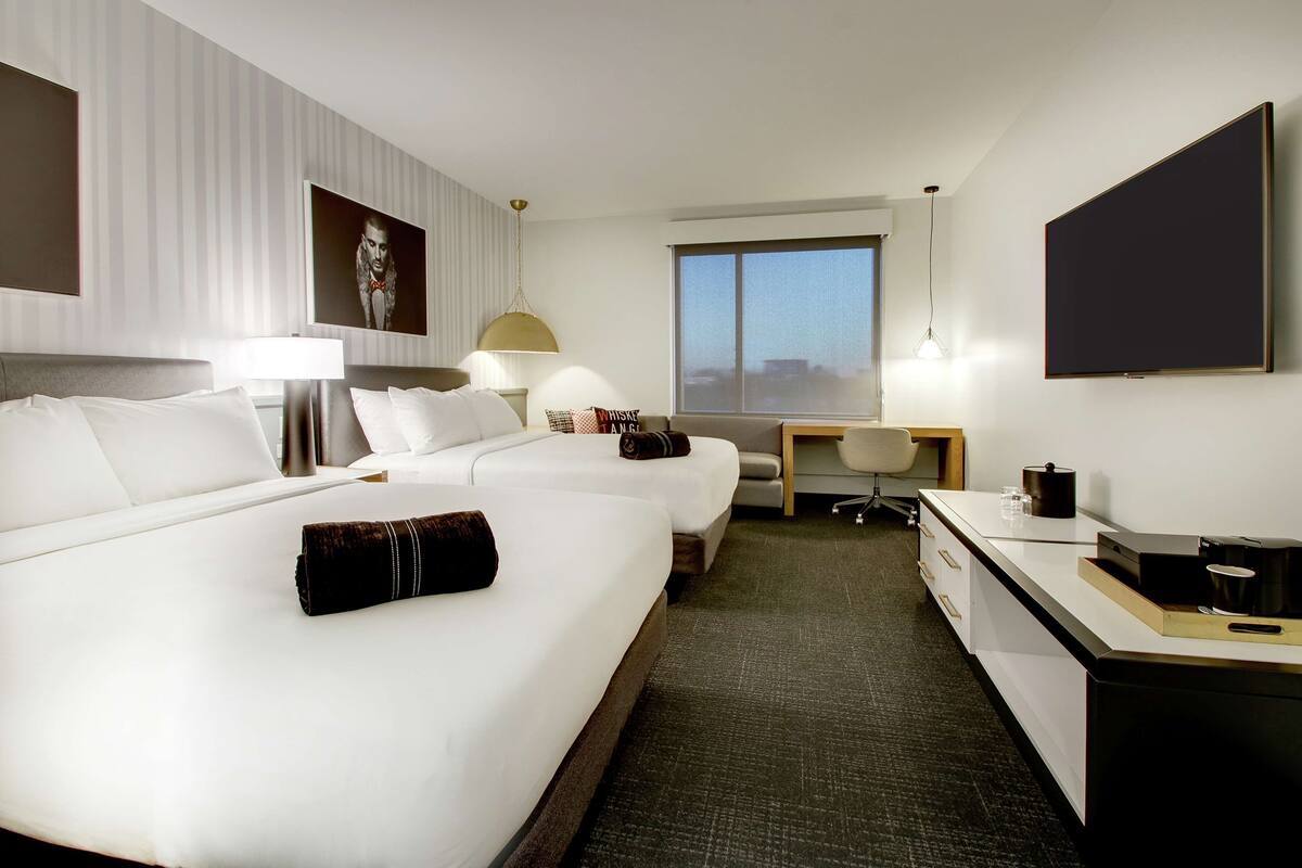 A hotel room with two beds, a desk, a chair, a flat-screen TV, and a window.