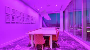 Een congreszaal met een lange tafel en stoelen, een glazen wand en kunstwerken aan de muur.