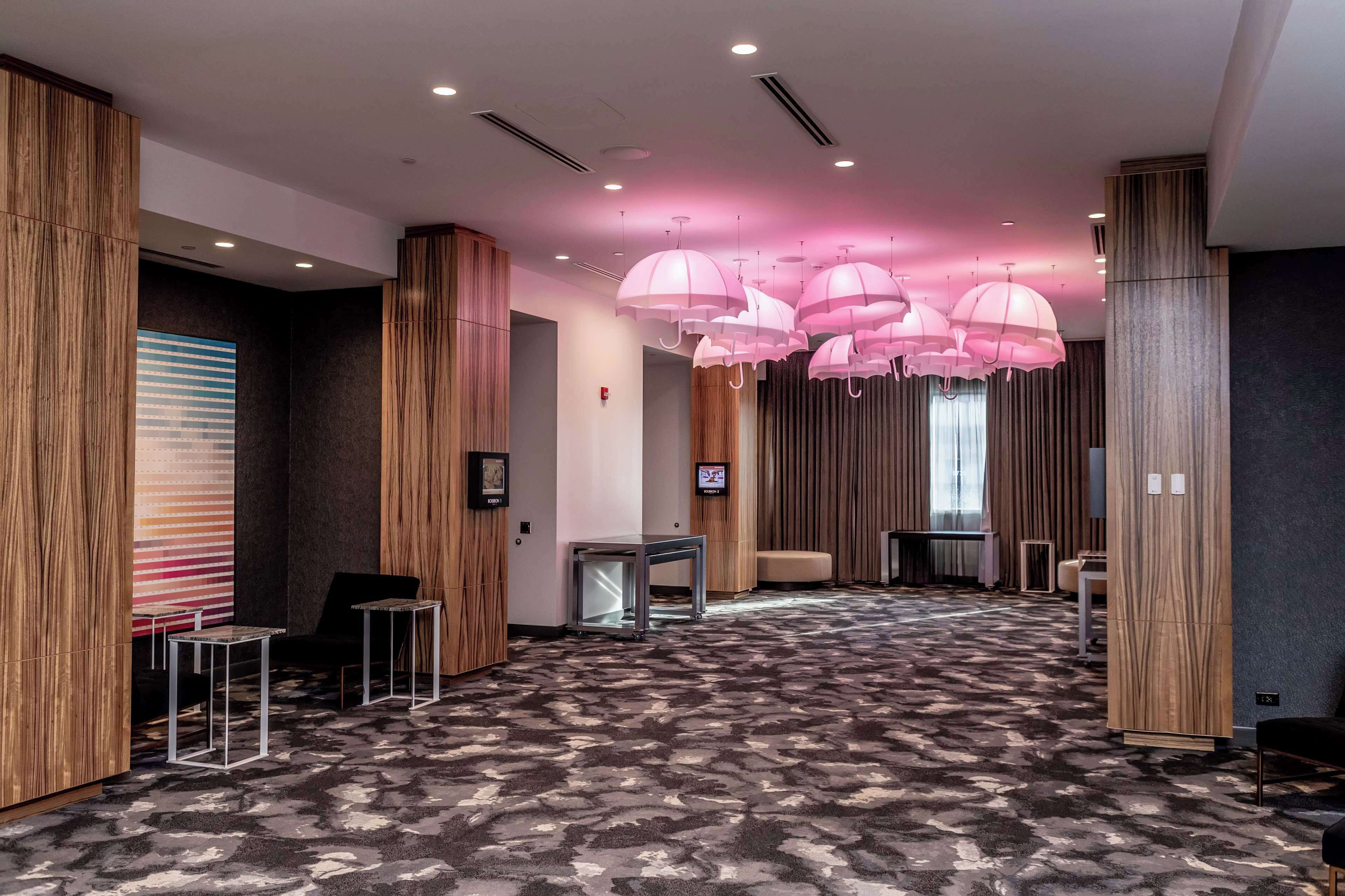 Un moderno vestíbulo de hotel con alfombra estampada, paneles de madera e iluminación colgante rosa.