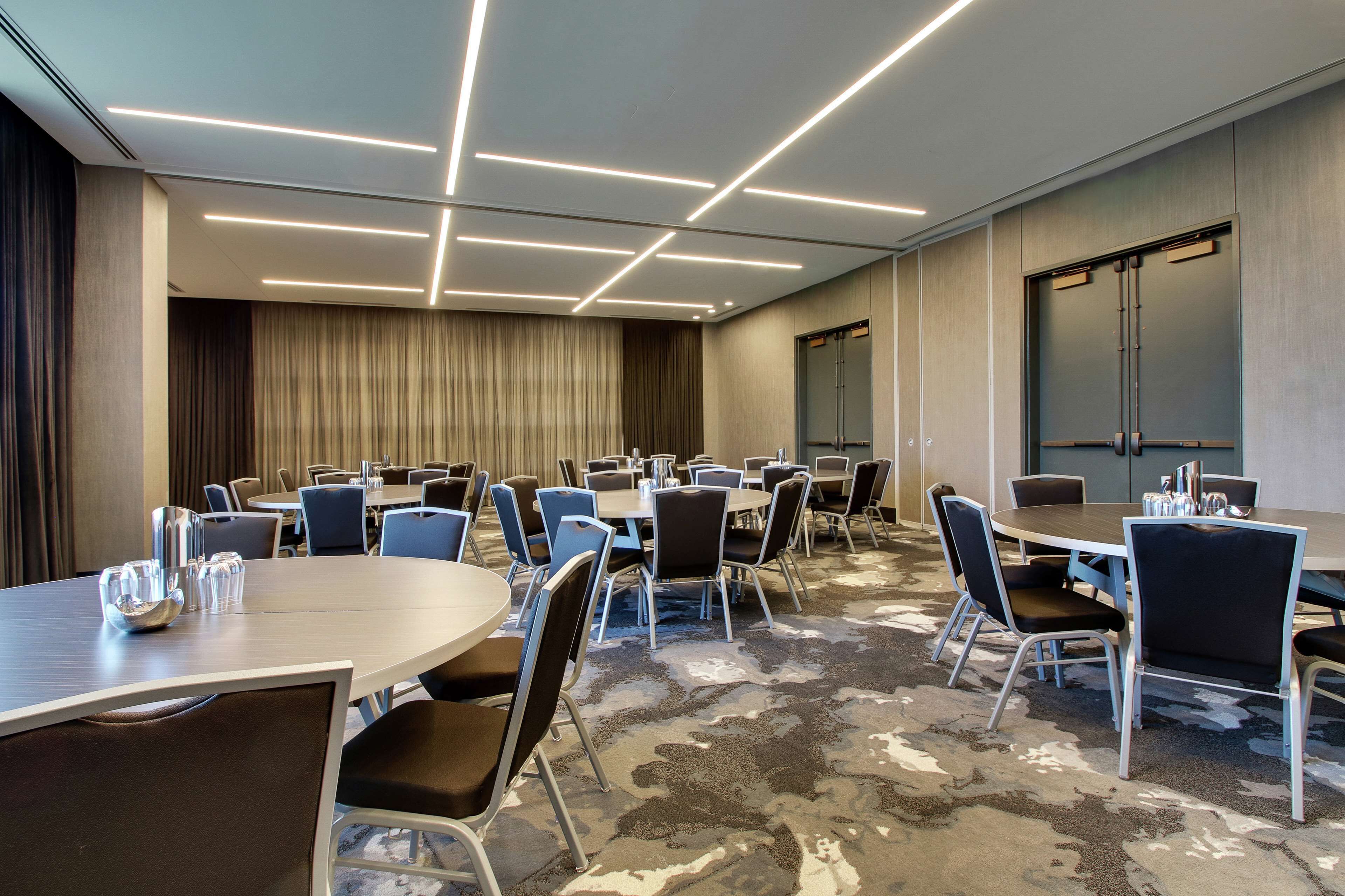 Un salón de conferencias con varias mesas y sillas, una alfombra estampada y un diseño de techo moderno.
