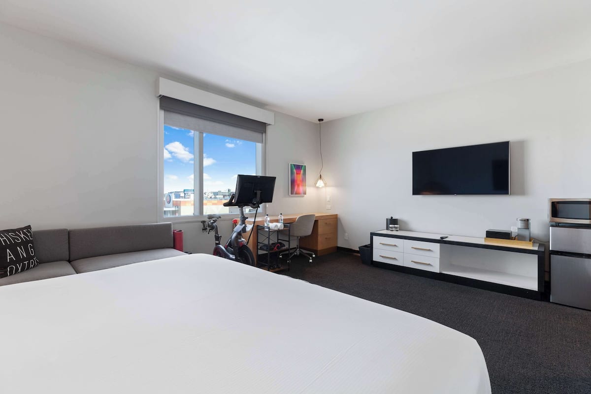 A modern hotel room with a large bed, a desk, a TV, and a view of the city.