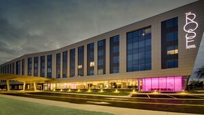 A modern hotel with a prominent neon sign, large windows, and a well-lit entrance area. - The Rose Chicago, Tapestry Collection by Hilton (Rosemont)