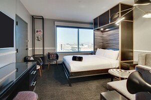 Una habitación de hotel moderna con una cama grande, un escritorio, una silla y vistas a la ciudad.