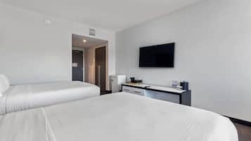 A hotel room with two beds, a desk, a flat-screen TV, and a mini-fridge.