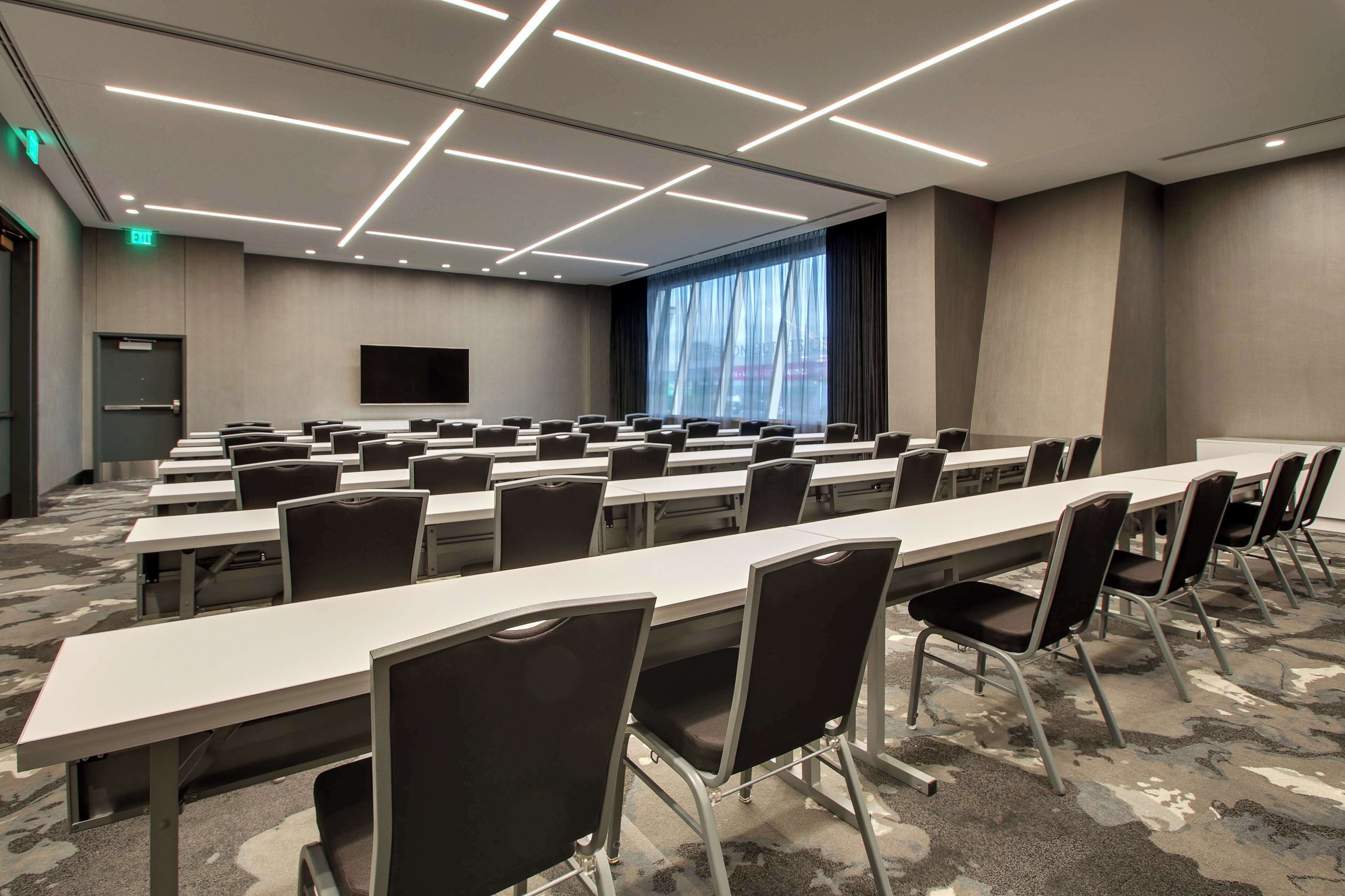 A conference room with long tables and chairs, a large screen, and a view of the city through large windows.